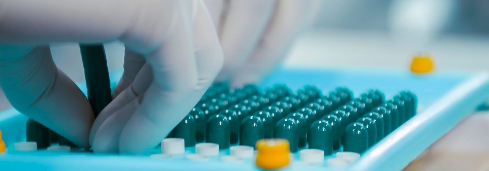 Close-up of gloved hands working with capsules in a pharmaceutical lab setting.