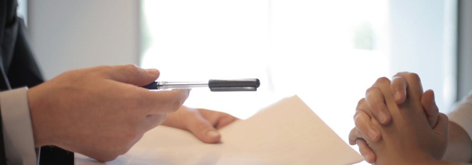 Side view of faceless formal man giving pen and paper to focused female with clenched hands at table on meeting