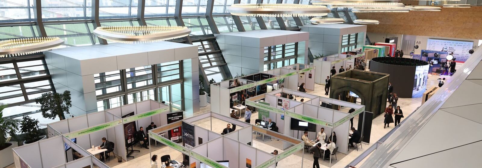 A bustling trade show exhibition inside a modern hall with people networking and exploring booths.